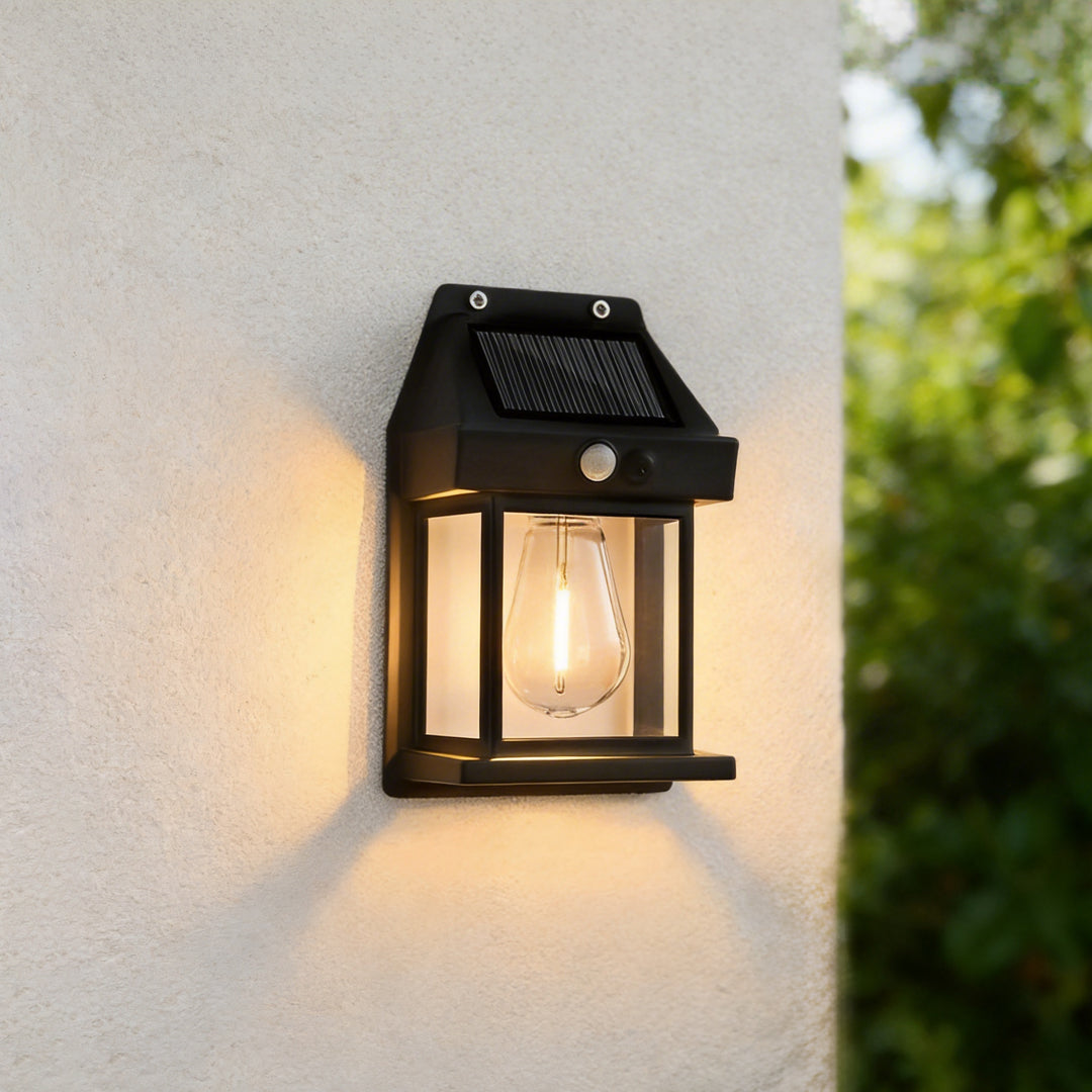 Close up of a wall mount solar lantern with a warm Edison bulb glowing on a beige stucco wall.