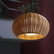 Close up of a woven rattan outdoor pendant light with a warm bulb glowing in a dark room setting.