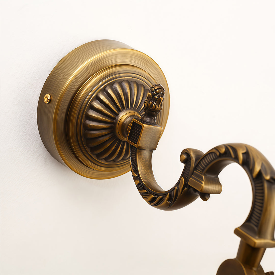 Close-up detail of bathroom LED vanity light showing ornate brass mounting bracket and curved arm.