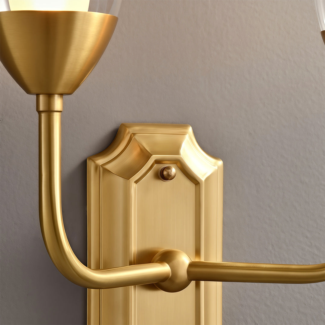 Close-up detail of glass wall light featuring glass shade chandelier styling highlighting polished brass construction and decorative backplate.