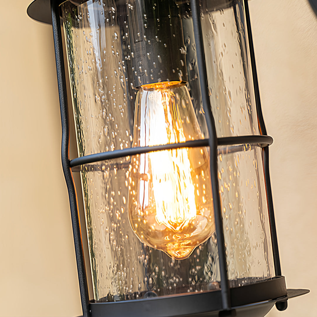 Close-up of outdoor wall mount light fixtures showing textured seeded glass and warm bulb.