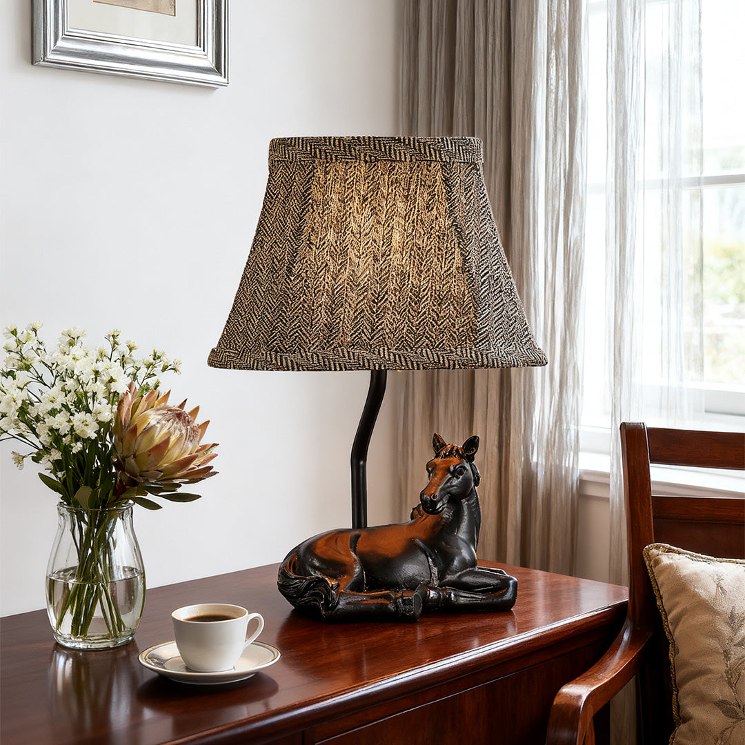 Close-up of the resin table lamp horse base and its patterned, brown-toned trapezoidal shade on a dining room sideboard.