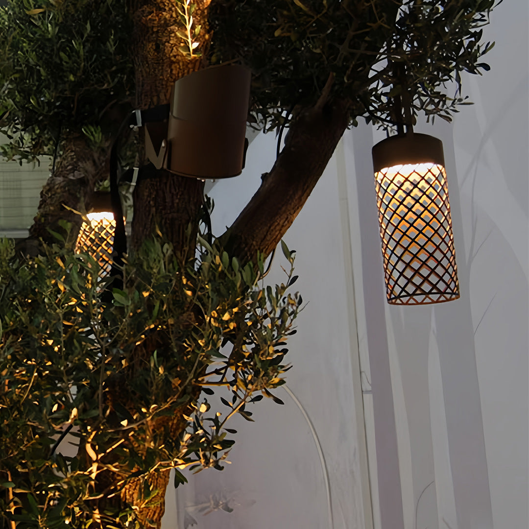 Close-up of the subtle texture and metal construction of the black outdoor pendant lantern hanging among olive tree leaves.