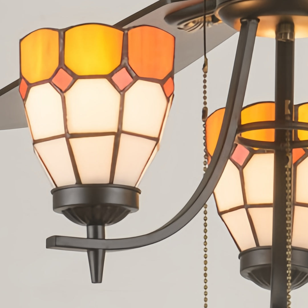 Close-up detail of vintage style ceiling fan light fixture with amber stained glass and bronze metalwork.
