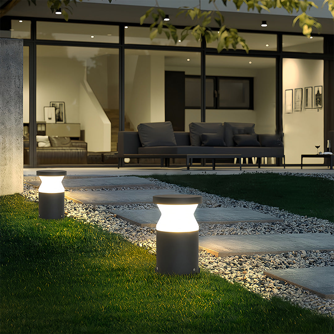 Close-up of a modern path lights fixture casting a warm yellow light onto a dark stone surface and surrounding garden plants.