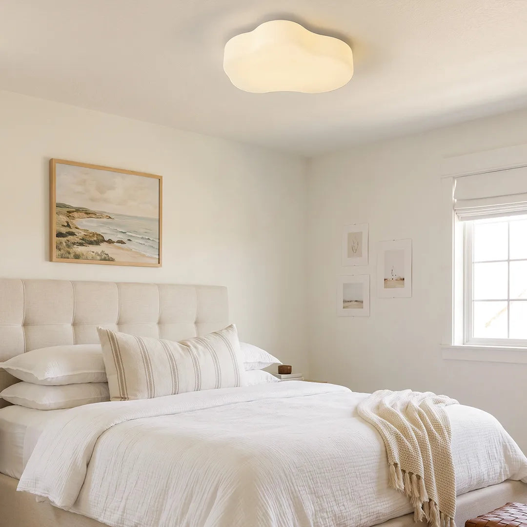 Cloud shaped ceiling light illuminating a soft white bedroom with a tufted bed and neutral decor.