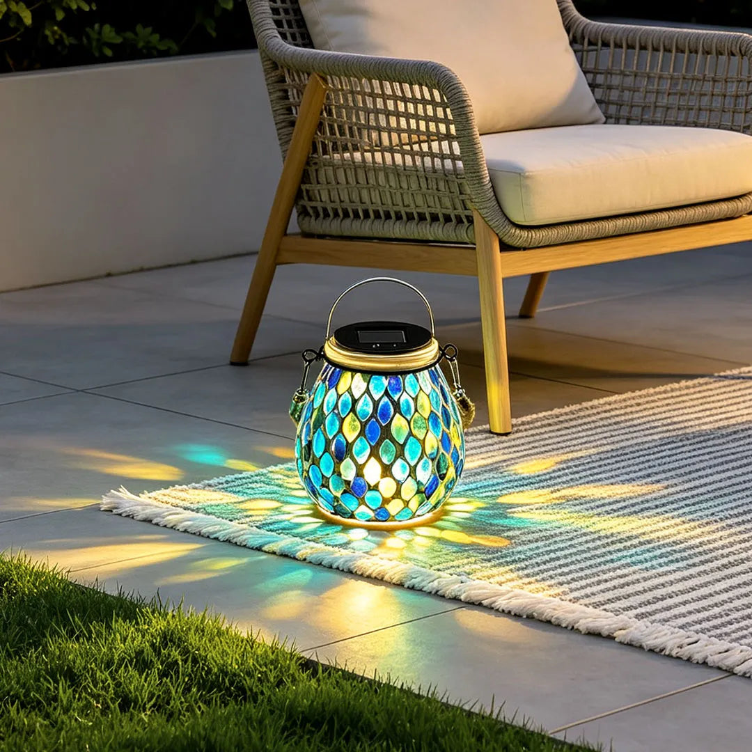 Colored landscape lights displaying a blue mosaic lantern on a patio rug near a woven outdoor chair.