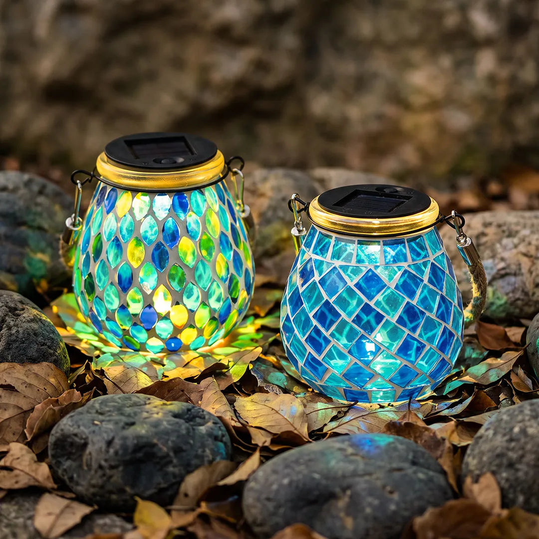 Colored landscape lights featuring two blue mosaic solar lanterns glowing among garden rocks.