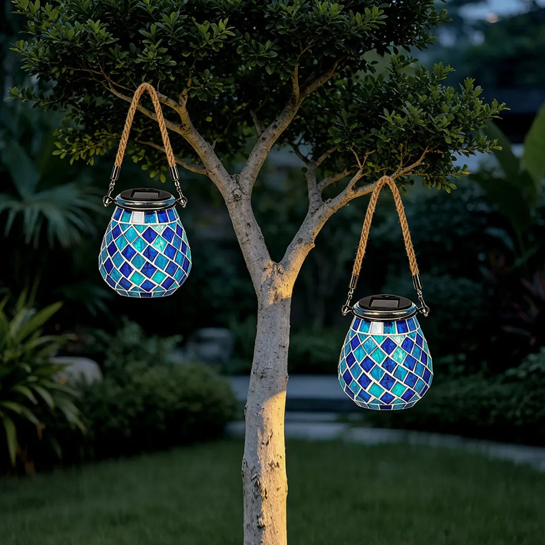 Colored landscape lights with two blue mosaic lanterns hanging from tree branches in a nighttime garden.