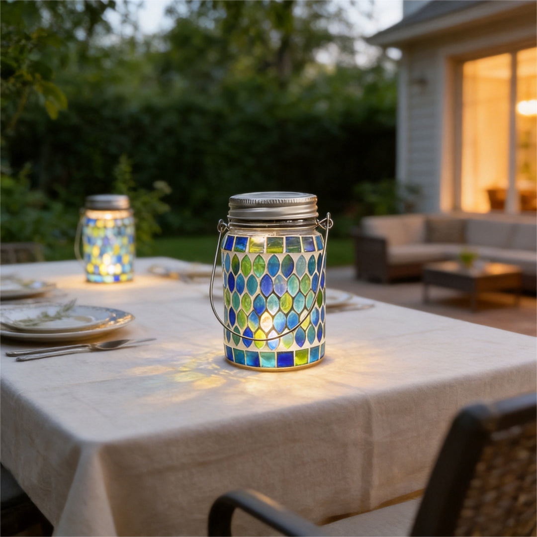 Colored landscape lights featuring a blue mosaic lantern placed on an outdoor dining table at dusk.