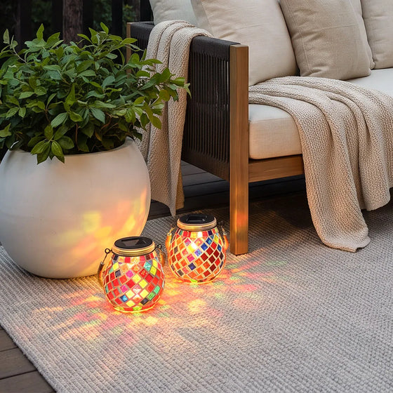 Colored landscape lights with two red mosaic lanterns casting patterned light beside an outdoor lounge chair.