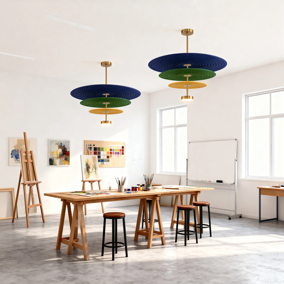 Two colorful 3 tier chandelier fixtures with blue, green, and yellow felt layers, suspended in a bright art studio workspace.