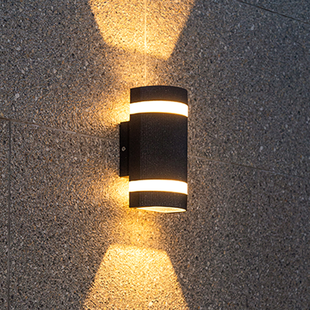Compact black garden wall light with dual openings casting warm light on tile