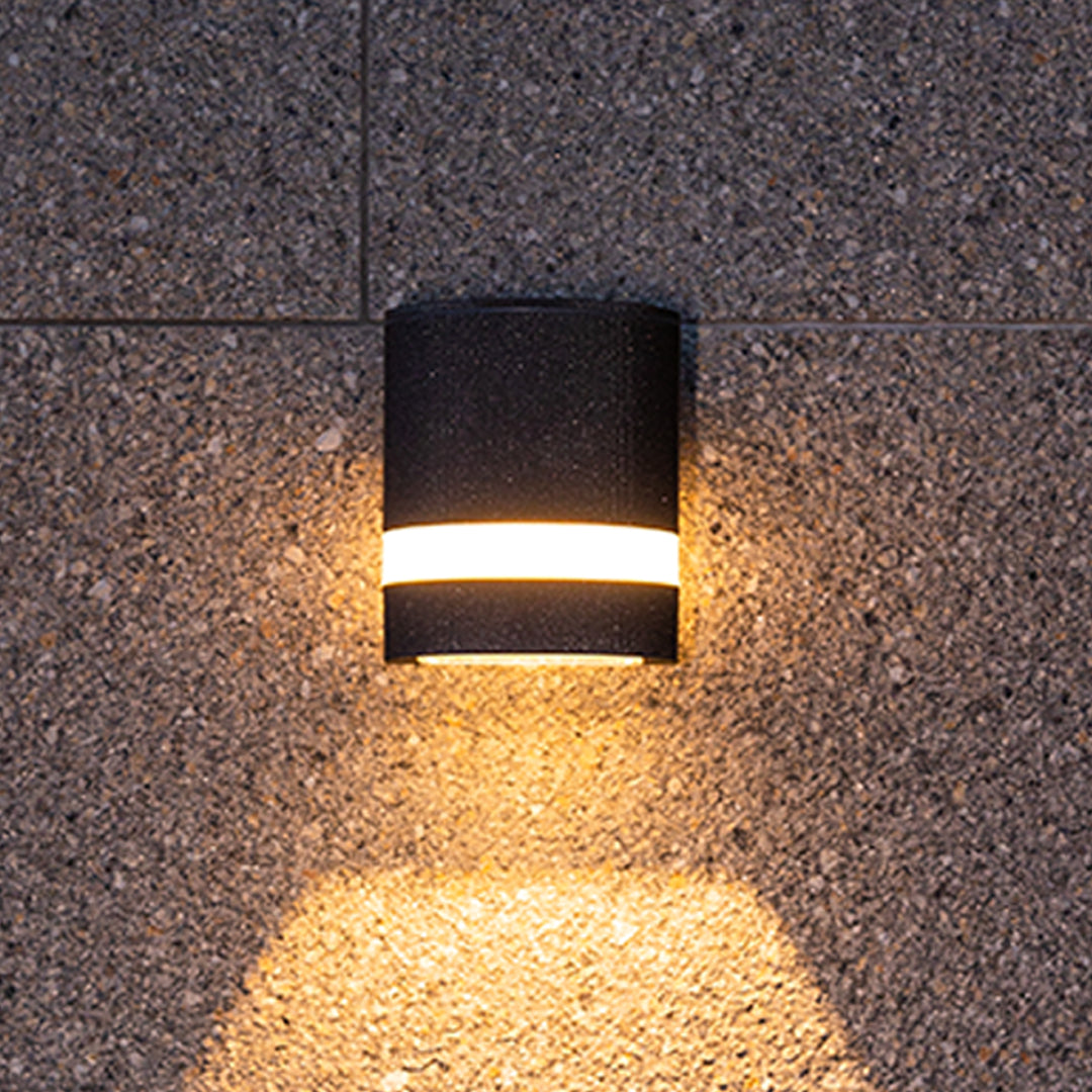 Compact black garden wall light with single horizontal stripe on dark textured wall