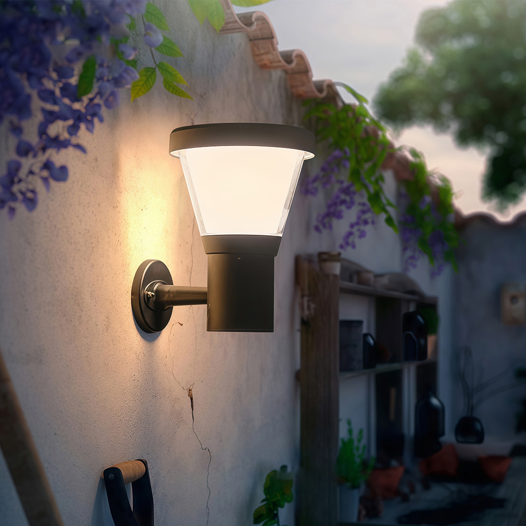 Compact black outdoor wall light mounted beside a gate, providing soft light for the entrance area.