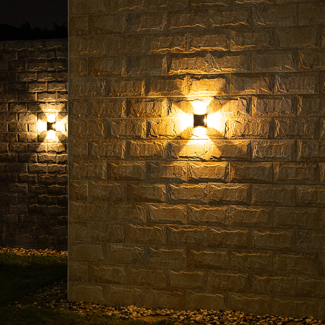 Compact black wall light producing striking four-directional beam pattern against modern exterior wall