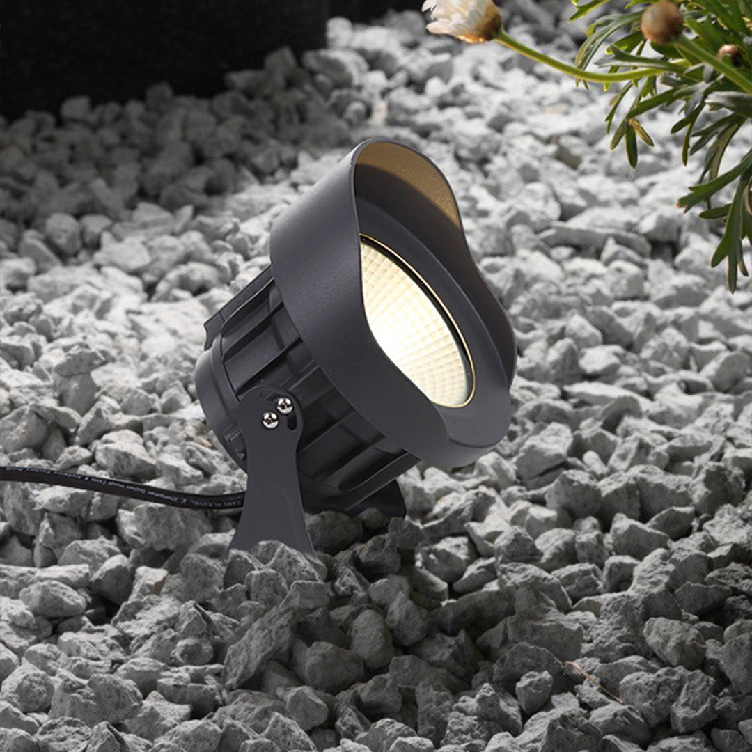 Compact black landscape light fixture positioned among decorative river rocks in garden setting