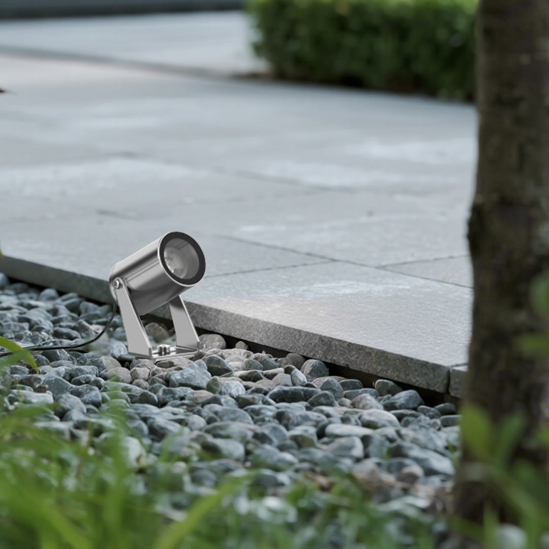 Compact landscape lighting spotlight fixture positioned among decorative stones for subtle pathway illumination