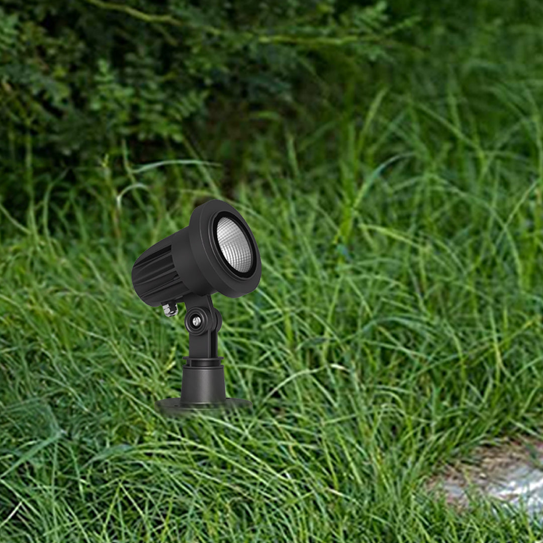 Small compact outdoor spotlight fixture embedded in lawn grass for ground-level illumination