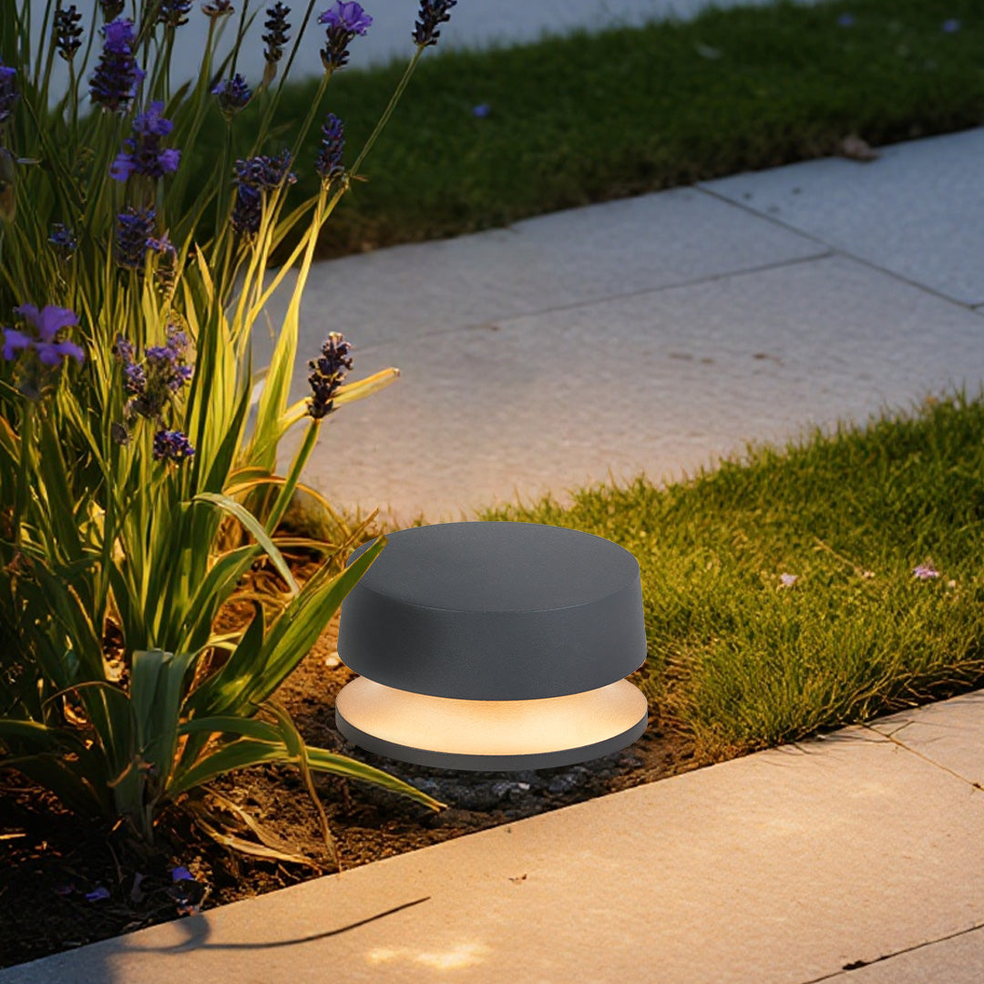 Round LED path light installed beside concrete pathway providing gentle guidance lighting through garden area