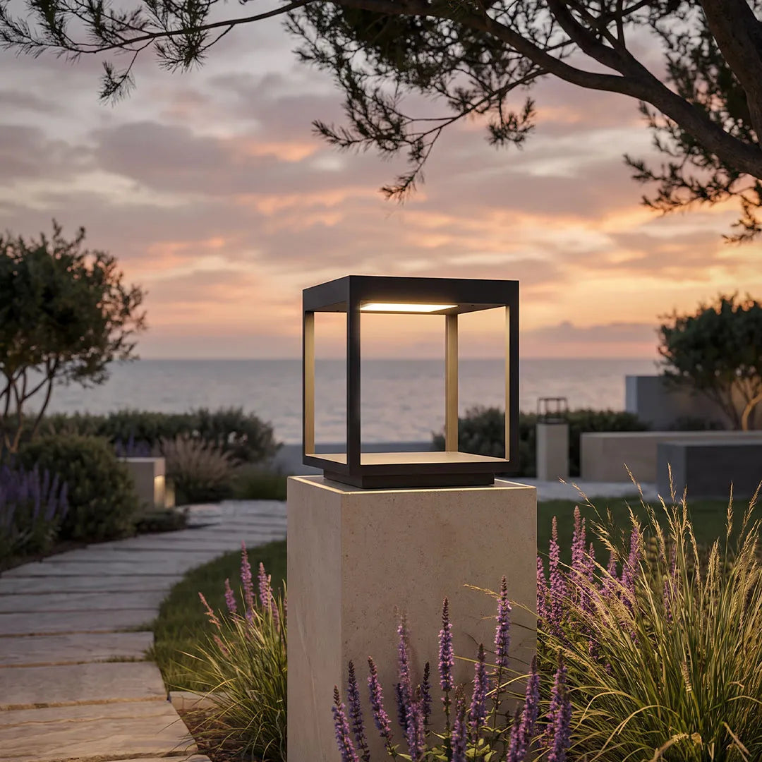 Concrete pillar light installed on a square outdoor column overlooking a landscaped garden at sunset.