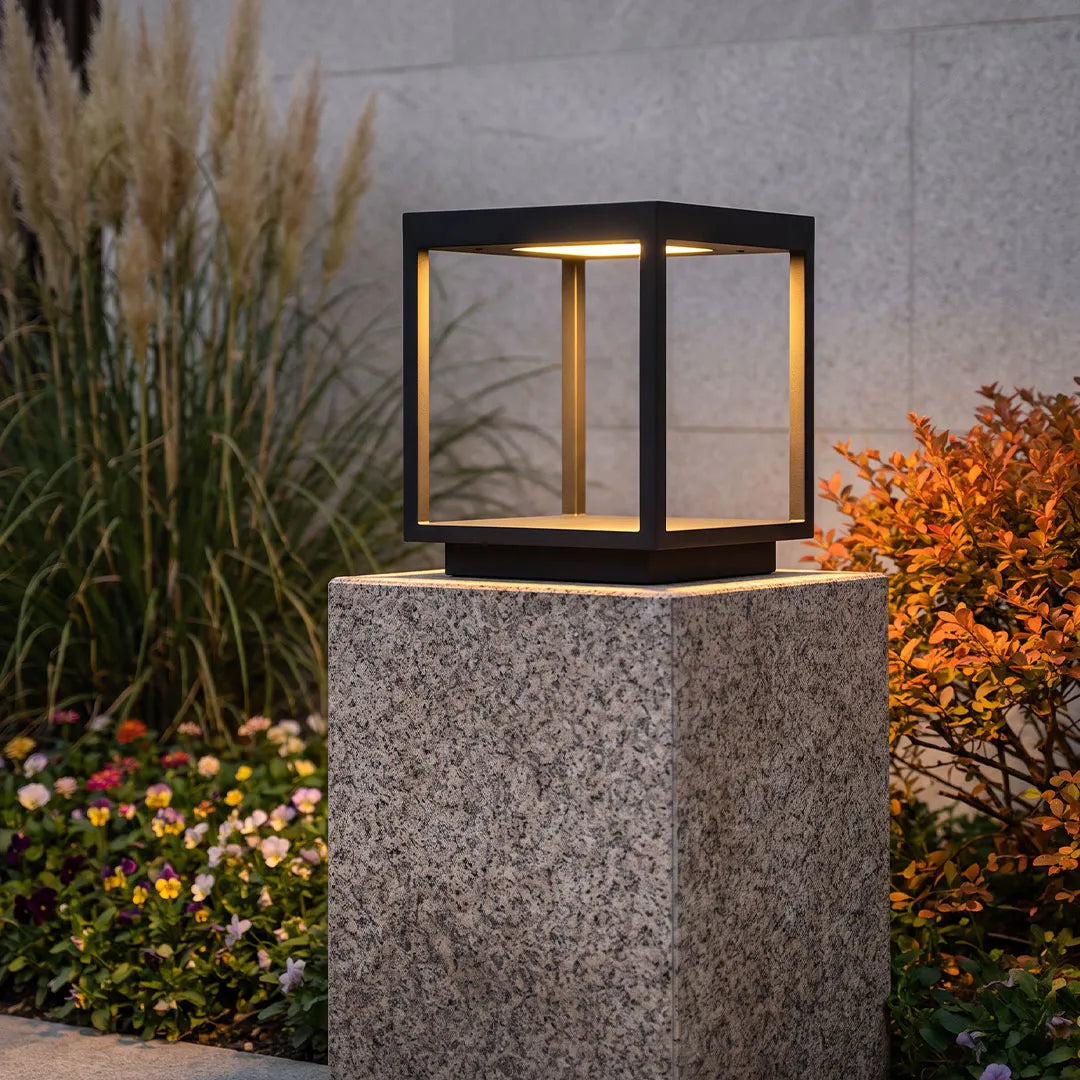 Concrete pillar light mounted on a textured stone post beside ornamental grasses and flowers.