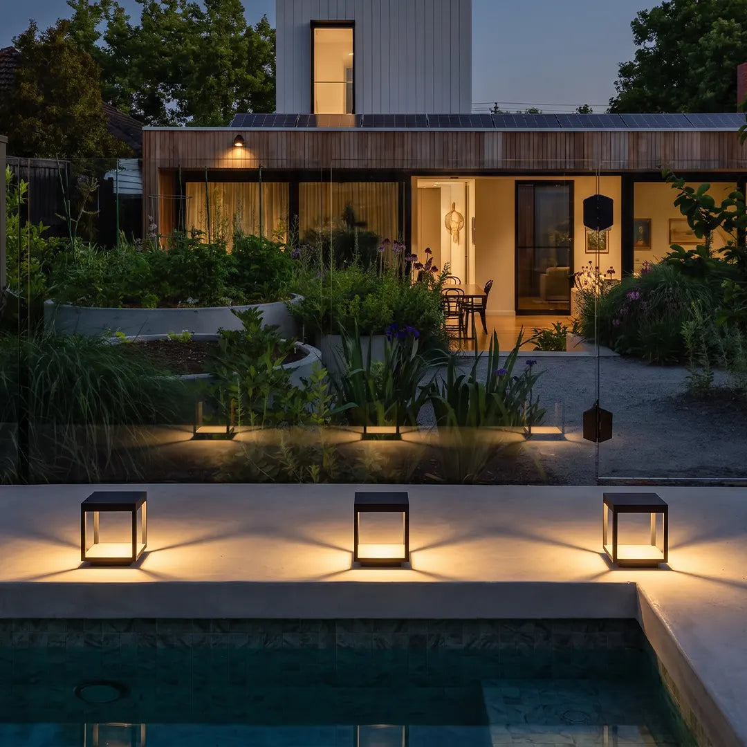 Concrete pillar lights lining the edge of a swimming pool in a contemporary backyard landscape at dusk.