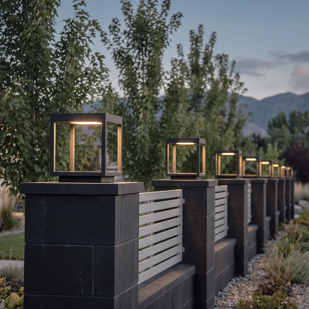 Concrete pillar lights arranged along a modern fence line with warm evening illumination.