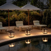 Concrete pillar lights illuminating a poolside patio with lounge chairs and umbrellas in a modern outdoor setting.