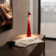 Cone shaped table lamp with warm light placed beside a window on a modern desk.