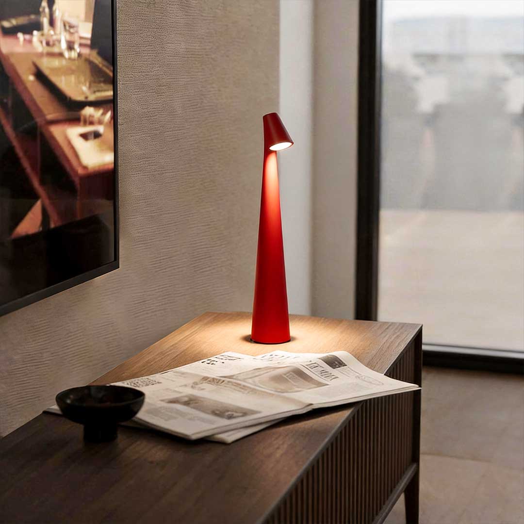 Cone shaped table lamp with warm light placed beside a window on a modern desk.