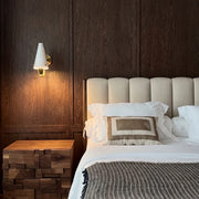 Cone wall light mounted beside a bed with a white tapered shade and warm ambient lighting.