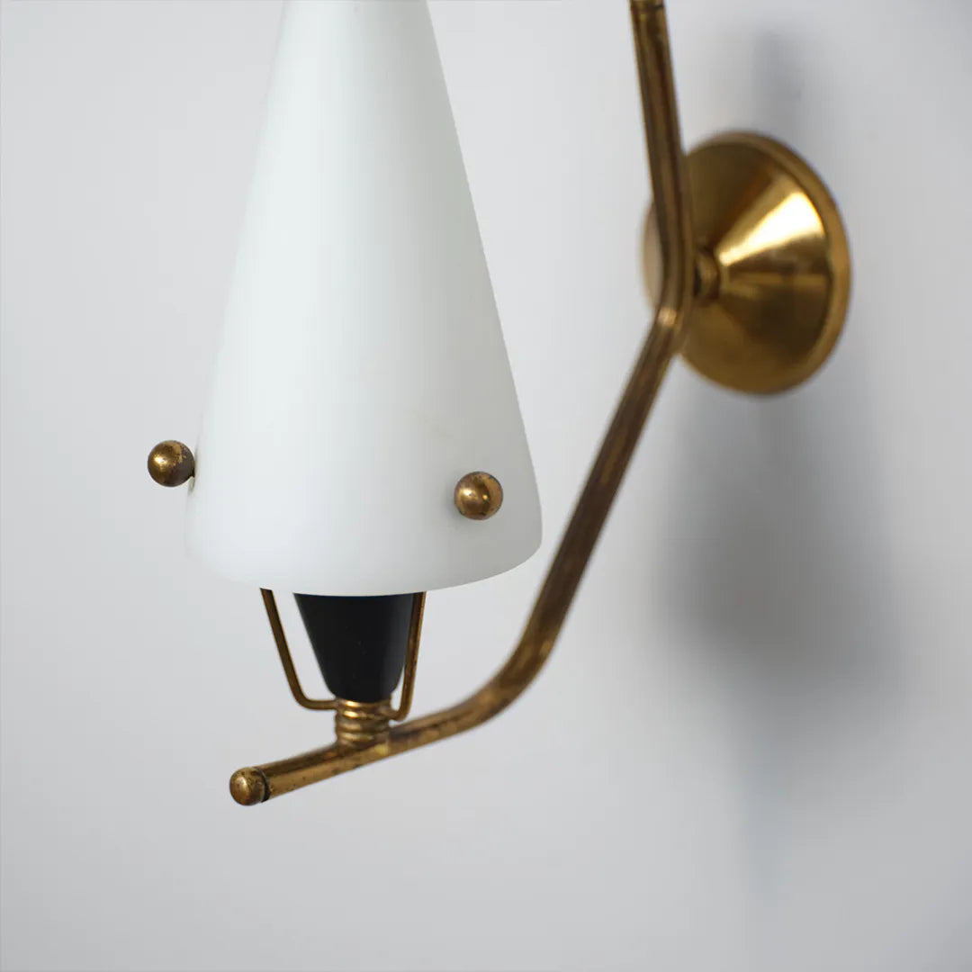 Cone wall light close-up showing the tapered shade, brass mounting plate, and curved fixture arm.