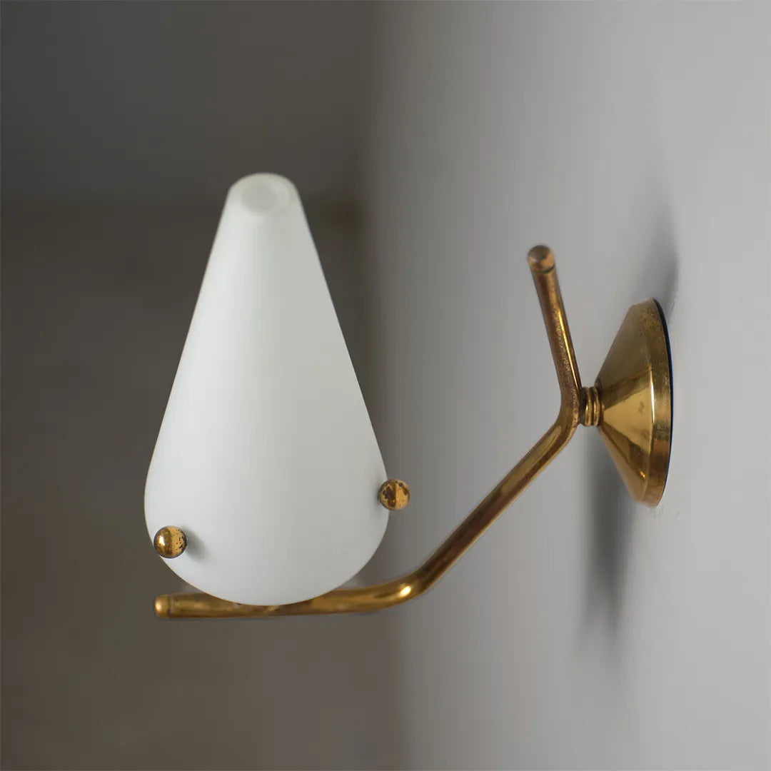 Cone wall light close-up showing the white conical glass shade and curved brass arm.
