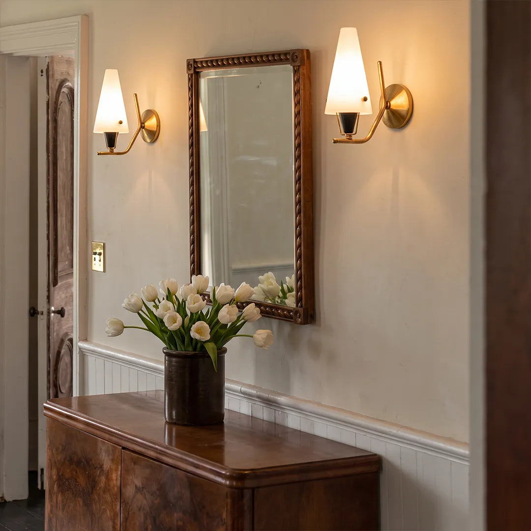 Cone wall lights mounted beside a mirror above a console table in an elegant interior.