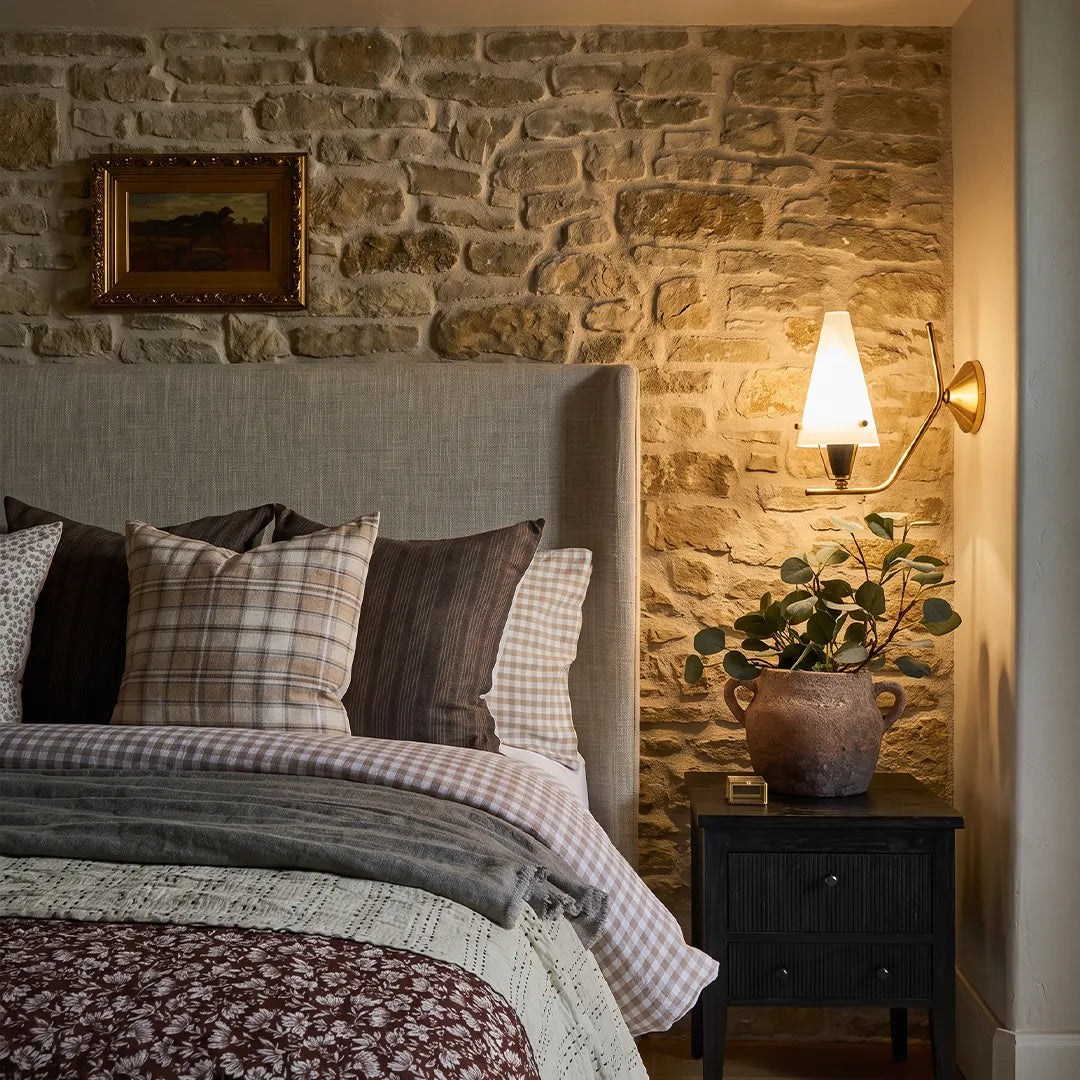 Cone wall light mounted beside a bed against a textured stone wall with cozy illumination.