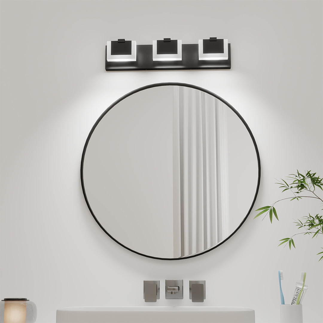 Contemporary bathroom LED vanity lights with glass shade chandelier influence mounted above round black mirror with plant accents.