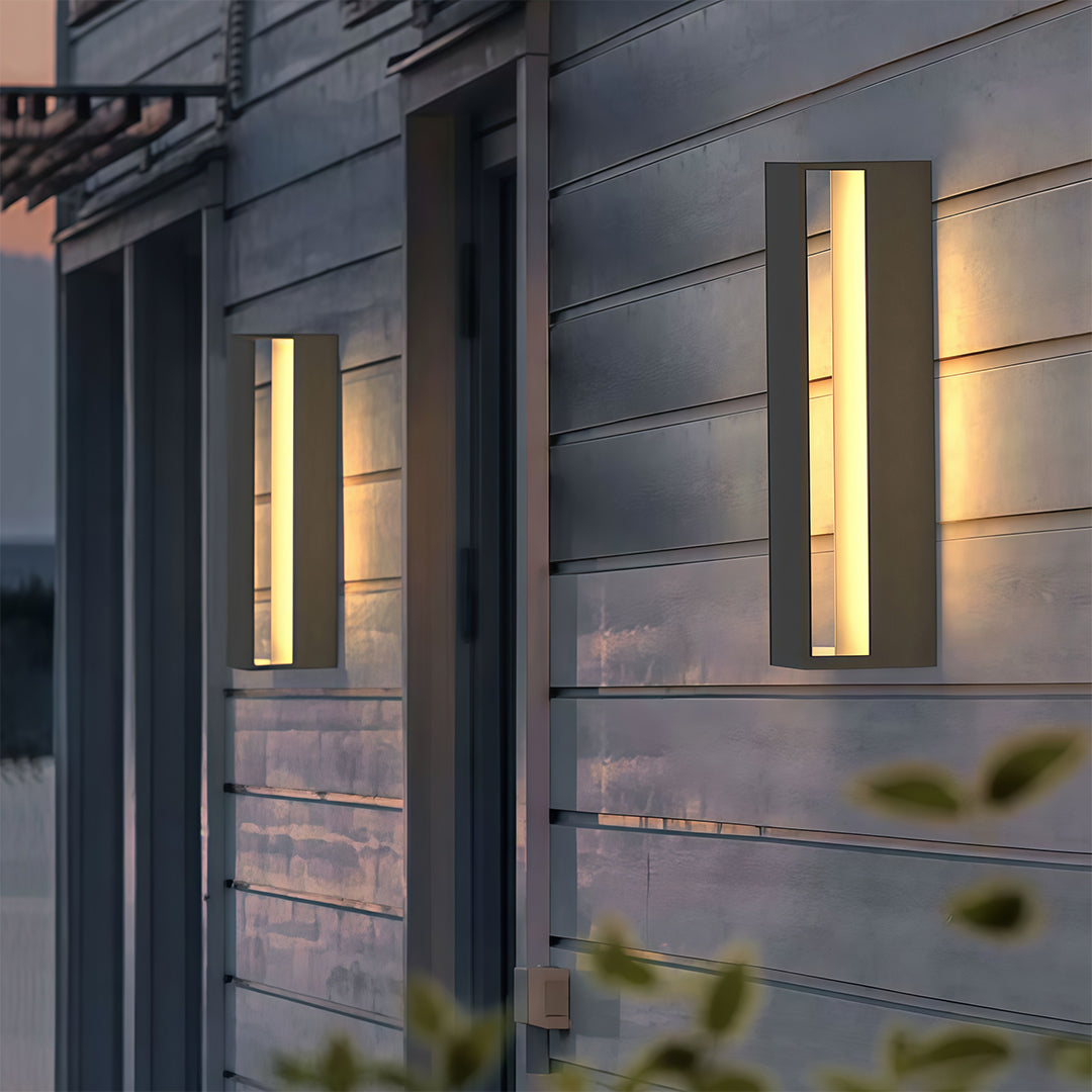 Contemporary black sconces outdoor with glass shade chandelier styling illuminating modern building facade with horizontal siding at dusk.