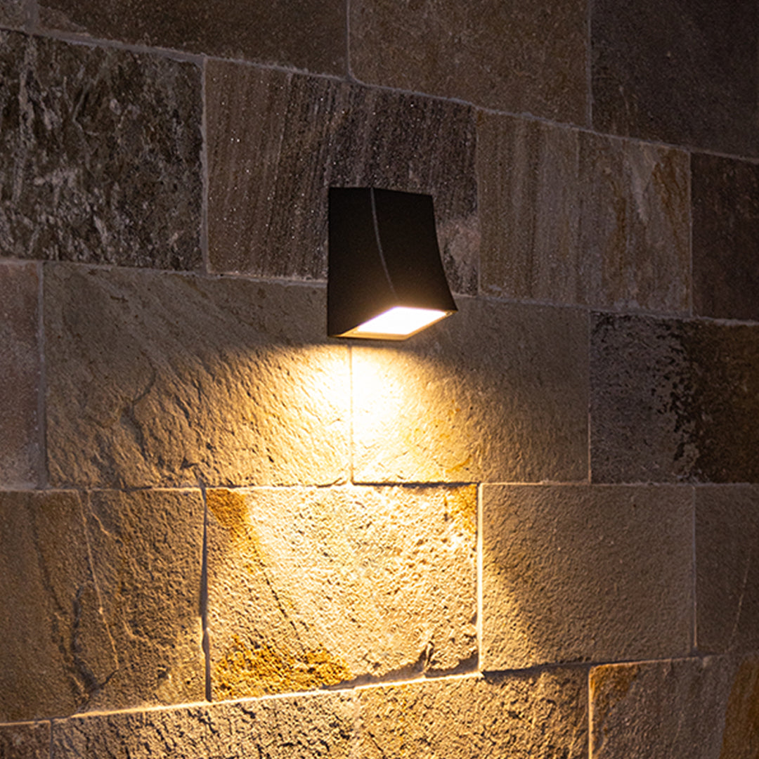 Contemporary black wall light illuminating textured stone surface with dramatic shadows
