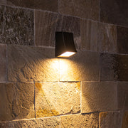 Contemporary black wall light illuminating textured stone surface with dramatic shadows