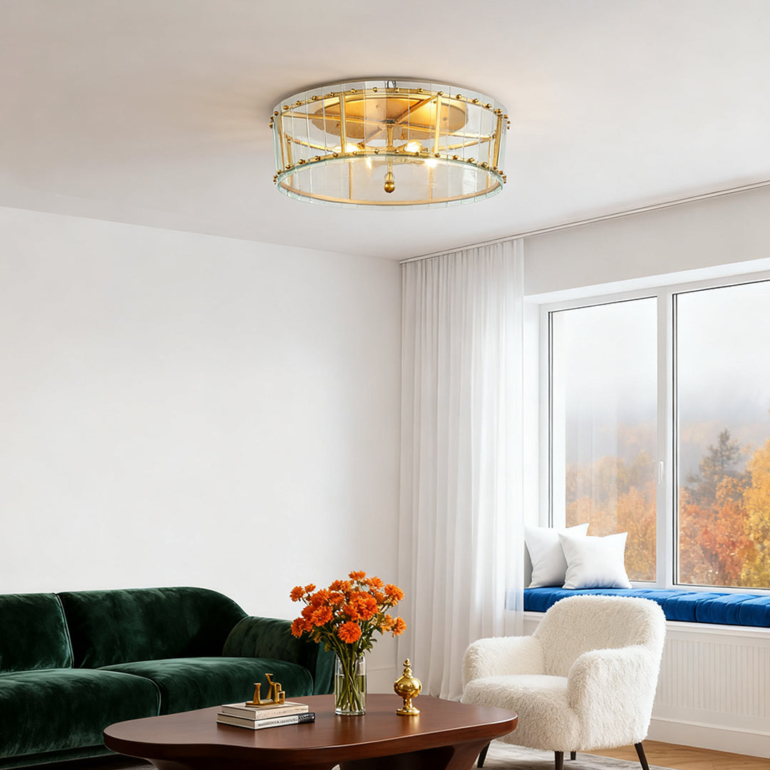 Contemporary flush mount gold light fixture in a bright living space with a dark green velvet sofa and large picture windows.