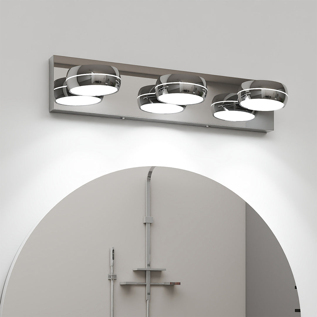Contemporary chrome bathroom vanity light featuring glass shade chandelier design installed above round mirror in neutral bathroom.