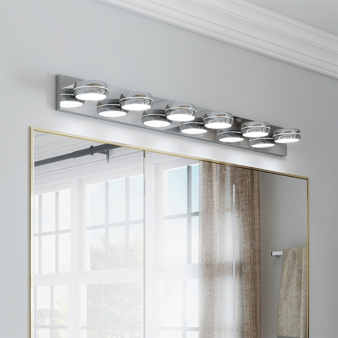 Contemporary chrome bathroom vanity light with glass shade chandelier aesthetic in clean white bathroom with curtained window.