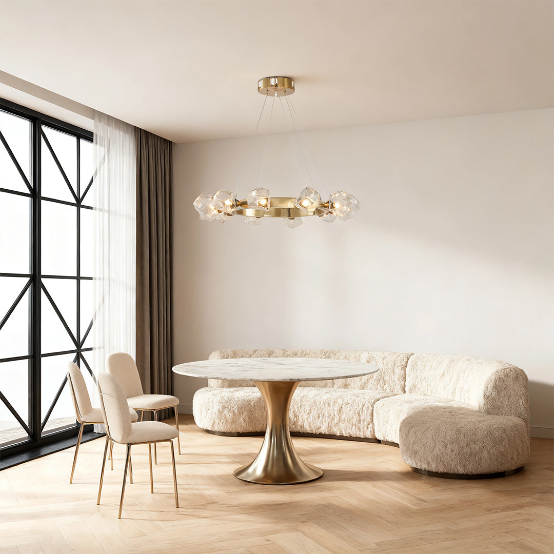 Contemporary seating area with a gold round chandelier hanging above a circular marble table and curved white sofa.