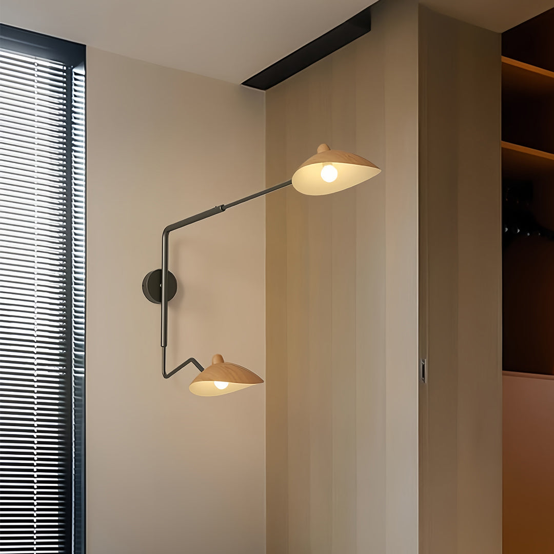 Contemporary double-jointed black swing arm wall light with two leaf-shaped shades, illuminating a light-toned bedroom corner.