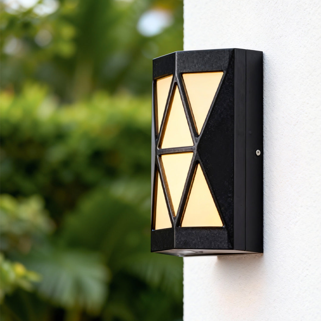 Contemporary outdoor wall sconces lighting mounted on an exterior wall beside greenery, casting warm ambient light.