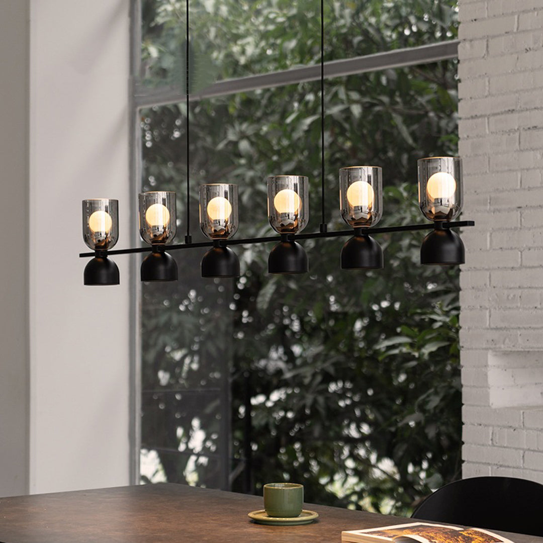 Contemporary glass pendant chandelier installed by a large window, featuring warm amber lighting and black metal frame.