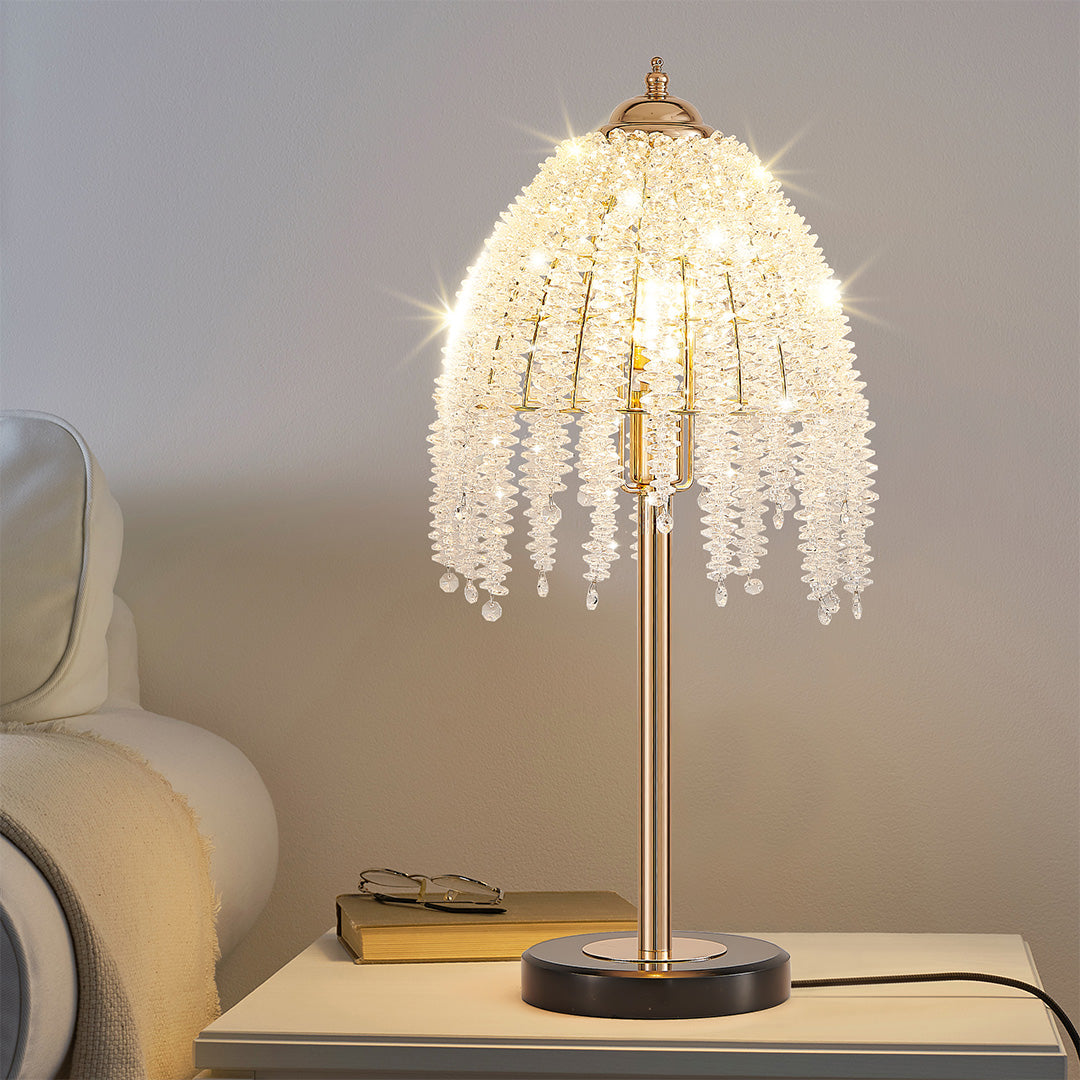 Contemporary gold bedside table lamp featuring glass shade chandelier aesthetic on modern round nightstand in neutral bedroom.