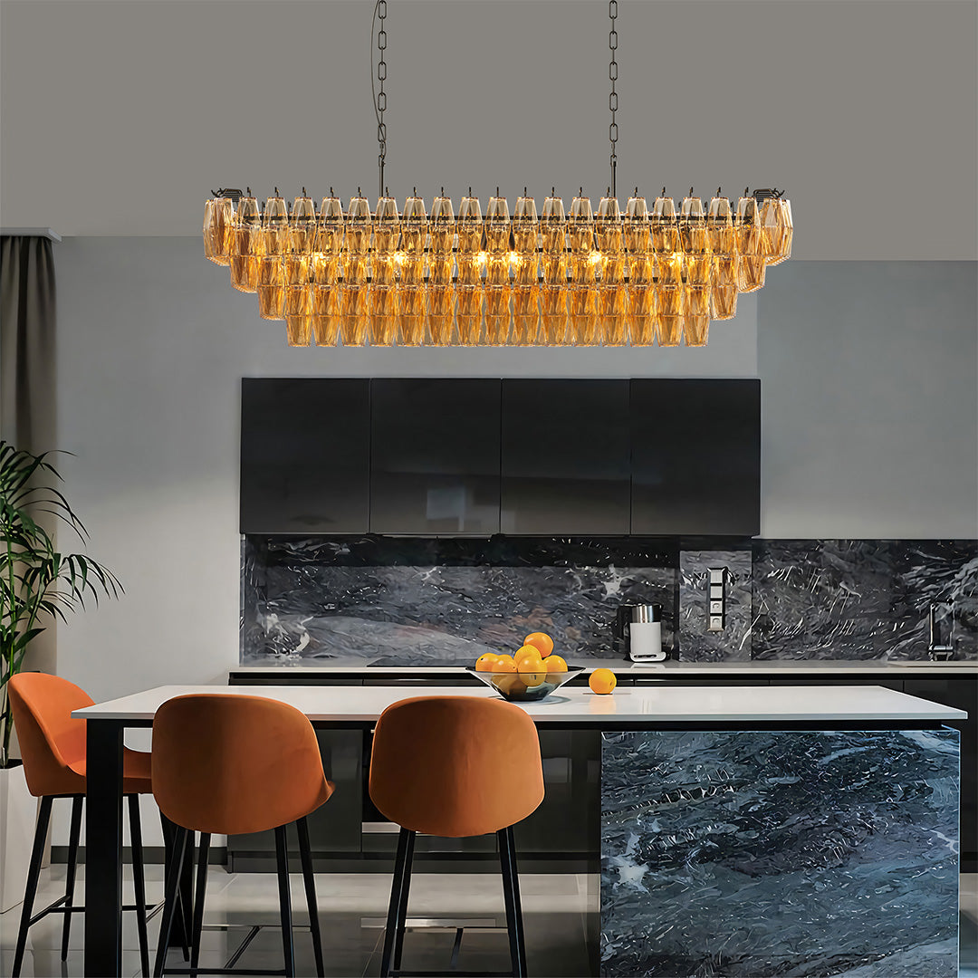 Contemporary gold glass pendant chandelier illuminating a sleek black-and-orange kitchen.