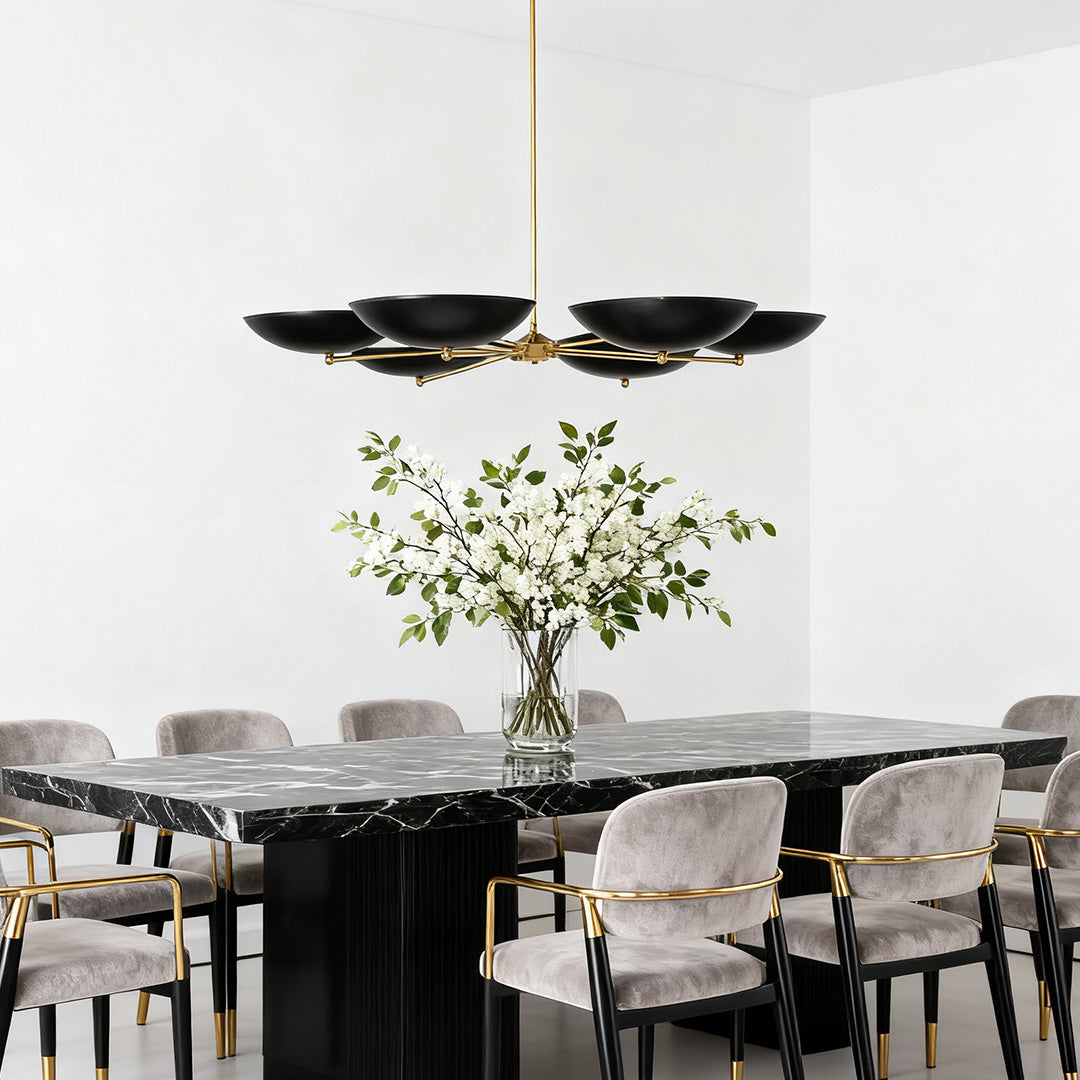 Contemporary black and gold chandeliers centered in a high-contrast white dining room with a large black marble table and velvet chairs.